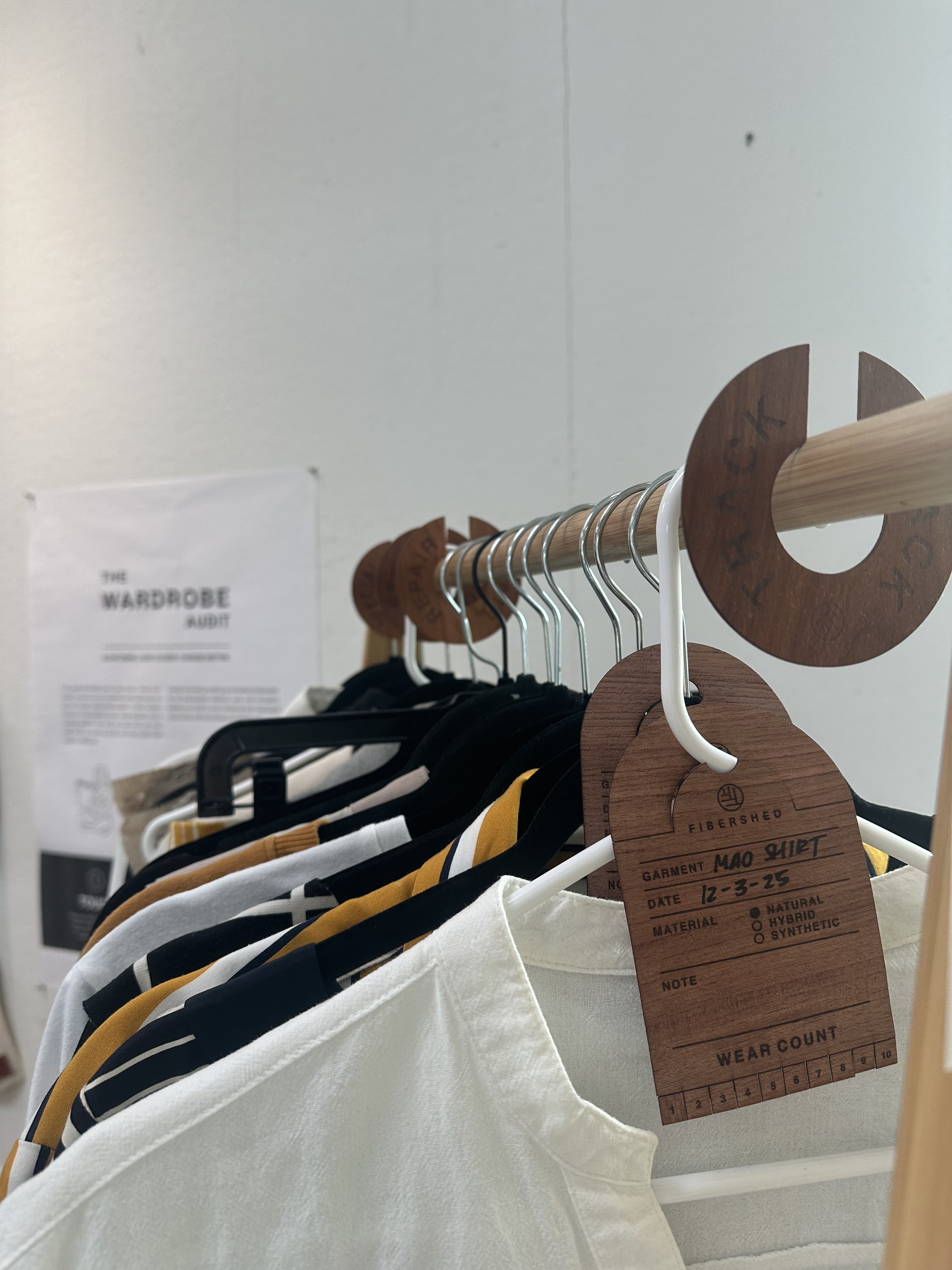 Wooden clothing rack holding shirts on hangers with hanging brown paper price tags